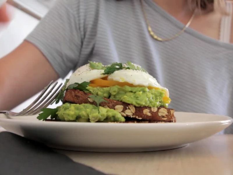 devojka jede vegetarijanski sendvič sa integralnim hlebom, avokadom i jajima