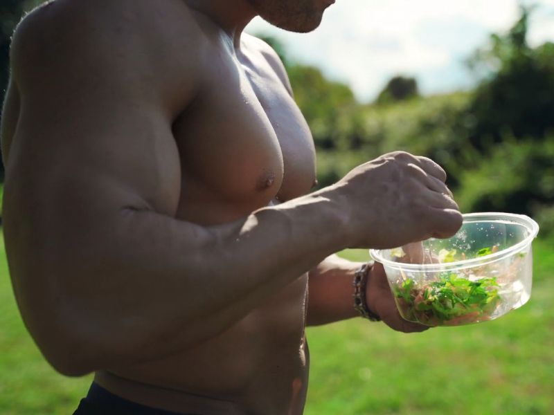 sportista bez majice jede salatu iz činije napolju