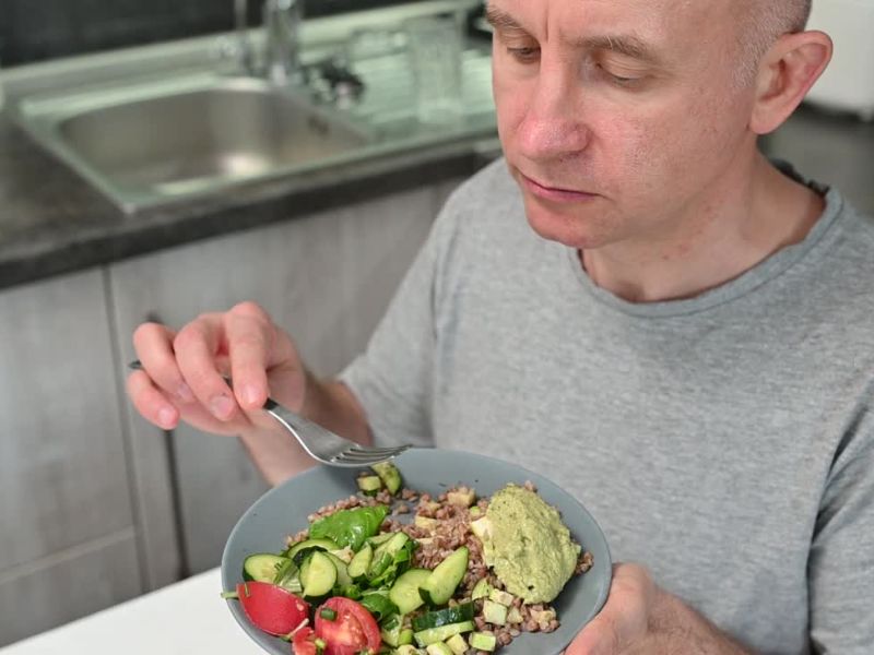 muškarac jede vegetarijanski obrok, salatu sa integralnim žitaricama i avokadom