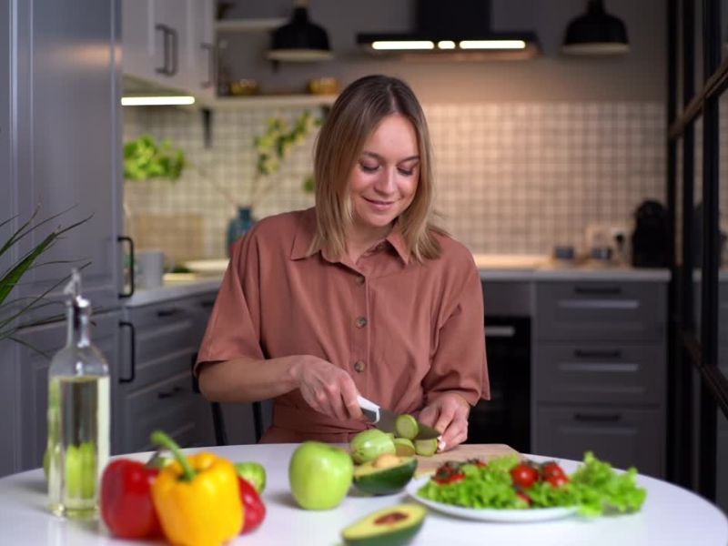 devojka seče tikvicu i sprema zdravu vegansku salatu, na stolu oko nje povrće i ulje