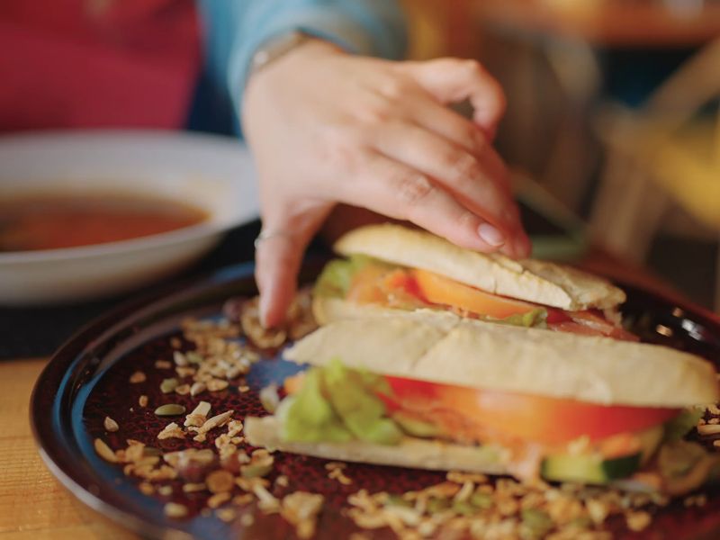osoba postavlja vegetarijanski sendvič i tanjir sa supom na sto